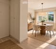 Modern dining area with a round wooden table surrounded by six light-colored chairs, a pendant light fixture, a sideboard with a vase and picture frames, and natural light from large windows.