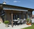 A modern house with a covered patio area featuring a dining set, potted plants, and a striped awning.