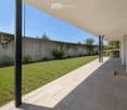 Modern outdoor patio with tiled flooring, covered roof, and a well-maintained lawn surrounded by a low concrete wall and greenery.