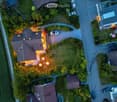 Aerial view of a residential area with multiple houses, well-lit driveways, parked cars, and landscaped gardens.