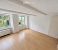 Empty room with wooden flooring, white walls, large windows, and a radiator. No furniture or equipment present.