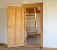 An empty room with wooden flooring and white walls, featuring an open wooden door leading to a closet with wooden shelves and a small ladder.