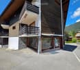 Modern two-story building with wooden and stone facade, multiple balconies, large windows, and a clear view of surrounding mountains.