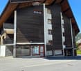 Modern two-story building with dark wooden facade, white concrete accents, large windows, and balconies.