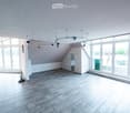 Bright, empty room with wooden flooring, large windows, and modern lighting fixtures. The space features white walls and a slanted ceiling typical of an attic or loft area.