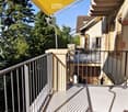 Balcony with metal railing, yellow awning, and view of trees and neighboring building.