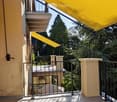 Balcony with a yellow awning, black metal railing, and a view of greenery.
