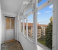 Empty room with large windows offering a view of the city and trees. The room has white walls, a wooden floor, and a door leading to another space.