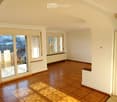 Empty room with wooden flooring, large windows, and a sliding glass door leading to a balcony with a city view.
