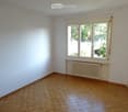 Empty room with wooden flooring, white walls, and large windows with a radiator below them.