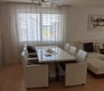 Bright living room with a sofa, coffee table, dining table, chairs, and a handbag on the floor. Large windows with white curtains and a modern painting on the wall.