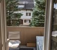Balcony with a chair, cushion, and flower box, overlooking a residential area with trees and a house.