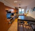 Modern kitchen with wooden cabinets, stainless steel appliances, a central island table with two stools, and a window offering a view.