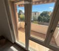 Open sliding glass doors lead to a tiled balcony with a metal railing, overlooking a residential area with trees and buildings.