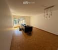 Living room with wooden herringbone flooring, white walls, large windows, and a black leather sofa.