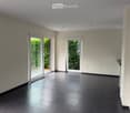 Empty room with dark tiled floor, white walls, and large glass sliding doors leading to a green outdoor area.