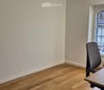 Empty room with wooden flooring, a single chair, and a table near a large window with a view of a building.