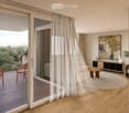 Modern living room with large windows and a view, featuring a sofa, coffee table, chairs, a cabinet, and artwork.