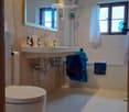 Modern bathroom with a toilet, double sink, bathtub, large mirror, and blue towels hanging on the side.