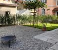 Garden area with gravel, a round black table, a potted plant, and a small wooden structure, surrounded by houses.