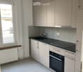 Modern kitchen with white cabinets, black countertops, a sink, a stove, and an oven. The space is well-lit with a window providing natural light.