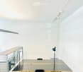 Modern, minimalist room with a large glass table, black chair, metal shelving unit, and track lighting.
