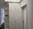 Empty hallway with white walls, a large built-in cabinet with open shelves and closed doors, and a skylight above. A door is visible on the right side.