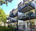 Multi-story residential building with multiple balconies, modern railings, and greenery around the base.