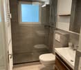 Modern bathroom with a glass-enclosed shower, toilet, sink, and built-in storage. Features include a radiator, a large window, and sleek fixtures.