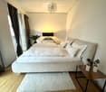 Modern bedroom with a large bed, nightstand, table lamp, side table with potted plants, and a view of a balcony.