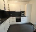 Modern kitchen with white cabinets, black countertops, stainless steel appliances, and a dark tiled floor.