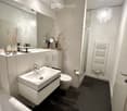 Modern bathroom with a white sink, toilet, large mirror, and decorative items on the counter. Features a glass-enclosed shower area and a white radiator.