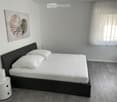 Modern bedroom with a double bed, white bedding, a nightstand with a lamp, and a contemporary painting on the wall.