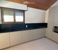 Modern kitchen with light-colored cabinets, black countertop, and stainless steel appliances including a sink and oven. Features a wooden-framed window and a wooden ceiling.