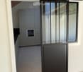 A modern sliding glass door with a black frame and glass panels, featuring a sleek design and a smooth, tiled floor in the hallway.