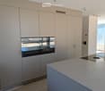 Modern kitchen with light-colored cabinets, a central island countertop, and a built-in oven with glass doors.
