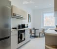 Modern kitchen with white cabinets, stainless steel appliances, a kitchen island, and a small dining area with a table and chairs.