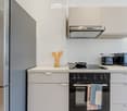 Modern kitchen with stainless steel appliances, white cabinets, and a light-colored countertop. Includes a refrigerator, oven, microwave, toaster, frying pan, wooden utensils, and kitchen towels.