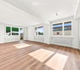 Empty room with wooden flooring, white walls, large windows, radiators, and a sliding glass door leading to a balcony.