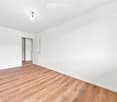 Empty room with white walls, wooden flooring, and a single open door leading to another room.