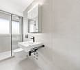 Modern bathroom with a white sink, toilet, mirror, and glass-enclosed shower area.