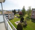 Balcony overlooking a green courtyard with trees, a picnic table, and surrounding buildings.