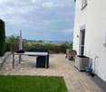 A modern patio area with a table, bench, umbrella, and storage box, surrounded by a neatly trimmed lawn and a white building.