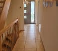 Hallway with tiled floor, wooden staircase railing, and modern lighting fixtures.