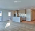 Modern kitchen with light-colored cabinets, a central island, and wooden flooring. Features include built-in appliances, ample natural light, and recessed ceiling lighting.