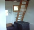 A narrow hallway with a wooden staircase leading upwards, carpeted steps, and a small window providing natural light.