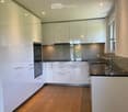 Modern kitchen with white cabinets, wooden flooring, stainless steel sink, and built-in oven.