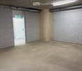Empty room with concrete floor, grey brick walls, wooden paneling, and a white door with an exit sign above it.