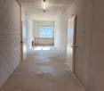Empty hallway with concrete walls and floor, white doors, a window at the end, and a fire extinguisher on the left side.