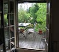 Balcony with wooden decking, glass sliding doors, table, chairs, and potted plants.